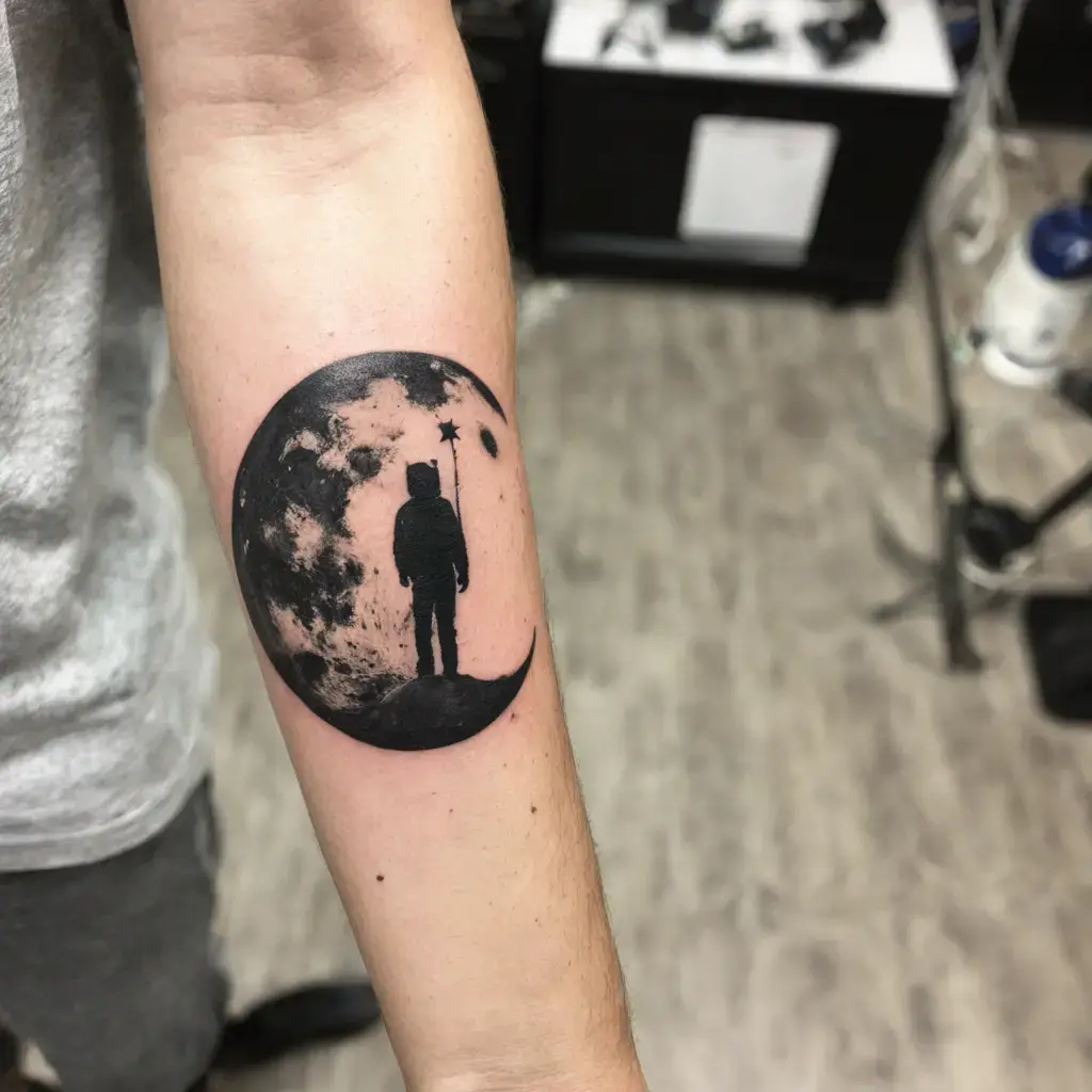 Minimalist black and white astronaut standing on a crescent moon forearm tattoo with star backdrop